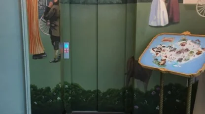 An elevator door painted to blend in with a mural depicting people in vintage clothing, next to a map on a stand and patterned floor tiles.