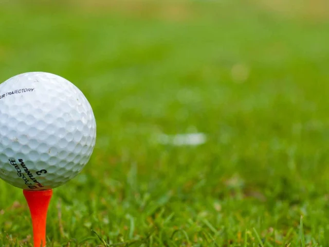 A white golf ball is balanced on an orange tee, set on green grass with a blurred background.