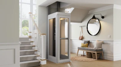 A modern home interior features a small residential elevator beside a staircase, with a bench, round mirror, and coat hooks in the entryway.