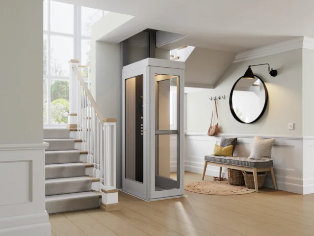 A modern home interior features a small residential elevator beside a staircase, with a bench, round mirror, and coat hooks in the entryway.