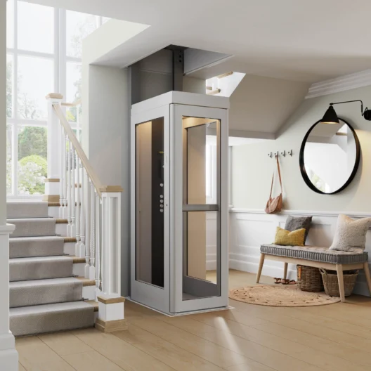 A modern residential elevator is installed next to a staircase in a bright, contemporary entryway with a bench, mirror, and coat hooks.