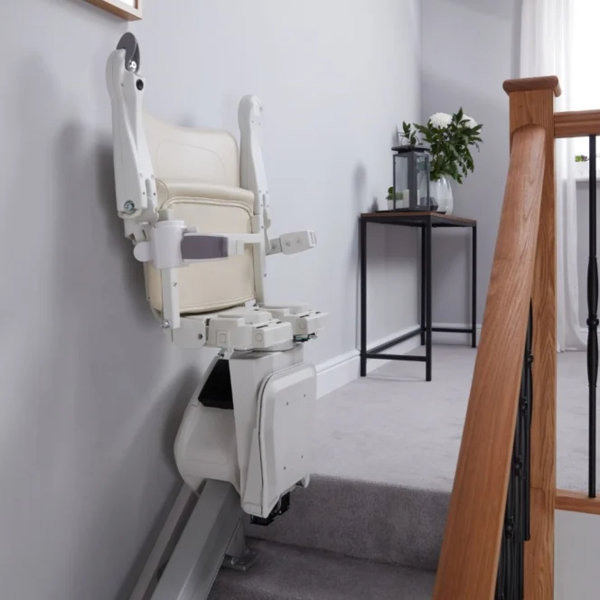 A stairlift with a white seat is installed along a carpeted staircase in a modern, light-colored home interior.
