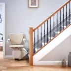 A modern stairlift is installed along a staircase in a bright, tidy home interior with wooden floors and minimalist decor.