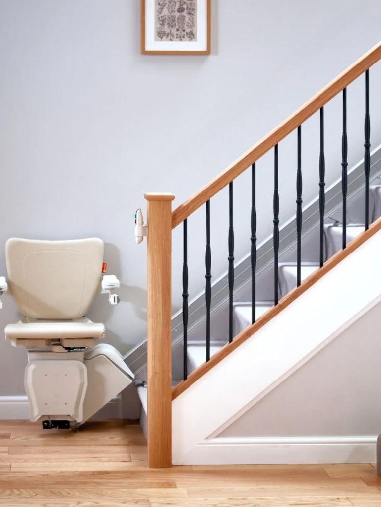 A modern stairlift is installed along a staircase in a bright, tidy home interior with wooden floors and minimalist decor.
