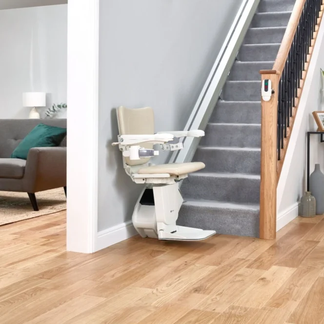 A stairlift is installed on a carpeted staircase in a modern home with wooden floors and neutral-colored furnishings.