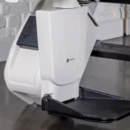 Close-up of a white stair lift motor unit and black footrest installed along a staircase in a modern interior with a brick wall.