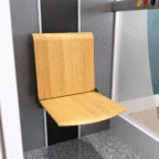 A wooden fold-down seat is mounted on a wall inside a modern elevator with gray walls and a speckled floor.