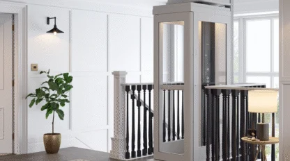 A modern residential elevator with glass panels is installed next to a staircase in a bright, carpeted hallway with white walls and black railings.