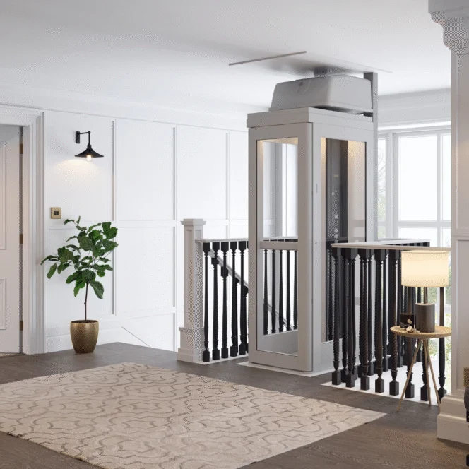 A modern residential elevator with glass panels is installed next to a staircase in a bright, carpeted hallway with white walls and black railings.