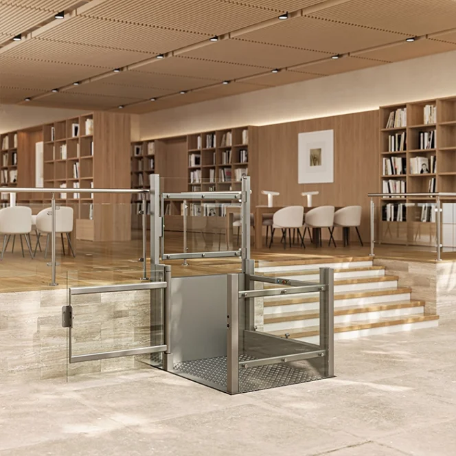 A wheelchair lift is installed beside a set of stairs in a modern library or lounge area with bookshelves and seating in the background.