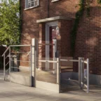 A residential brick building entrance features an outdoor wheelchair lift beside stairs, with metal railings and glass panels, allowing accessible entry.