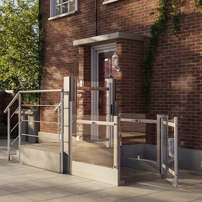 A residential brick building entrance features an outdoor wheelchair lift beside stairs, with metal railings and glass panels, allowing accessible entry.