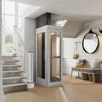 A compact residential elevator is installed beside a staircase in a modern, well-lit home entryway with a bench, mirror, and coat hooks.