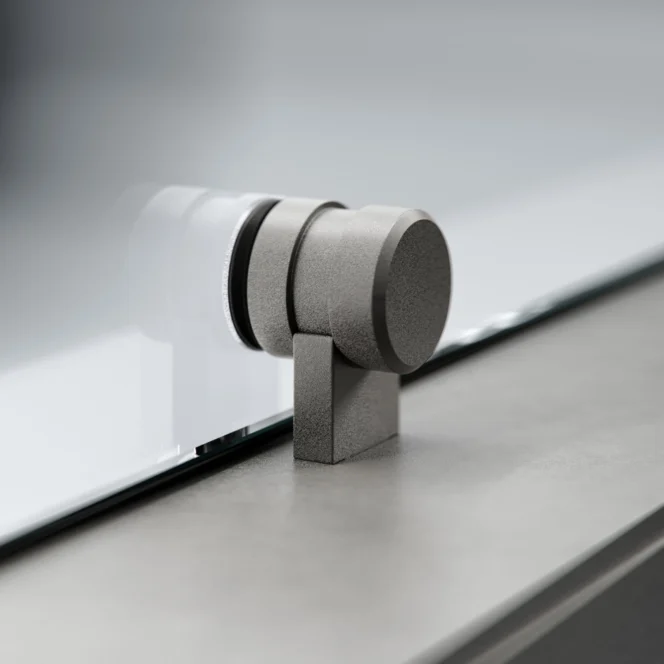 A close-up of a metallic hinge or support bracket attached to a glass panel, mounted on a smooth, gray surface.