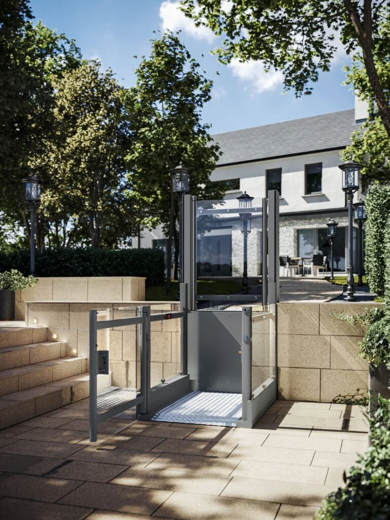 A modern outdoor wheelchair lift is installed beside stone steps, providing accessible entry to a patio area near a contemporary house.