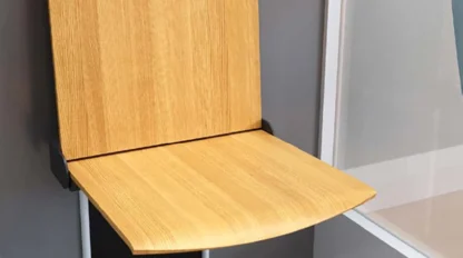A wooden folding chair attached to a wall, shown in an open position against a gray and white background.