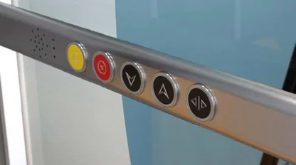 Close-up of five elevator control buttons, including emergency and floor selection buttons, set in a metallic panel.