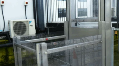 A metal and glass outdoor platform lift is installed next to a building with steps, providing wheelchair accessibility.