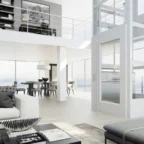 Modern open-plan living area with floor-to-ceiling windows, white decor, a home elevator, and a view of the city skyline. Dining area and upper loft visible in the background.