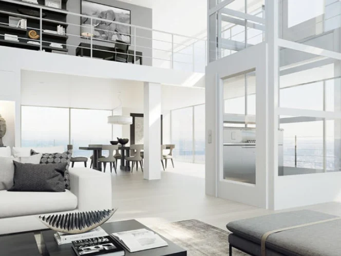 Modern open-plan living area with floor-to-ceiling windows, white decor, a home elevator, and a view of the city skyline. Dining area and upper loft visible in the background.
