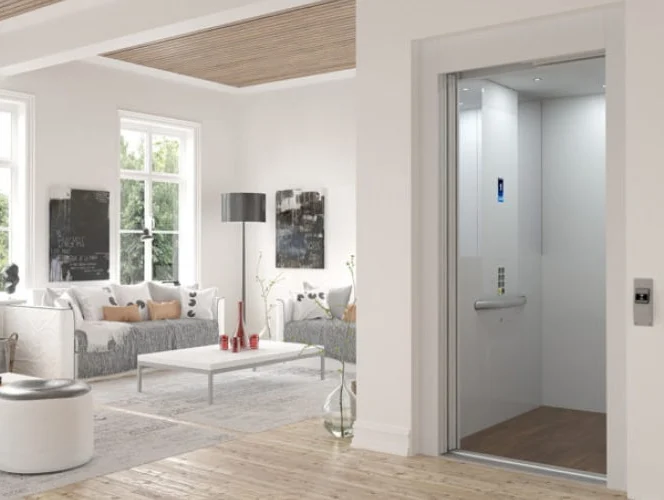 A modern living room with large windows and minimalist decor features a residential elevator with open doors next to a white wall.