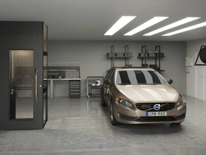 A tan Volvo sedan is parked in a modern, clean garage with workbenches, tool cabinets, and overhead lighting.