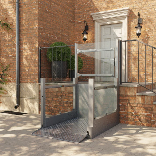 A modern outdoor wheelchair lift is installed beside brick steps, providing accessible entry to a raised doorway of a brick building.