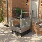 A vertical platform lift is installed next to stairs outside a brick building, providing wheelchair access to the elevated entrance.