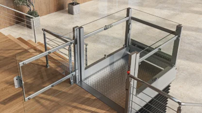 A modern wheelchair lift with glass panels is installed next to a staircase in an indoor public building with elevators and potted plants.