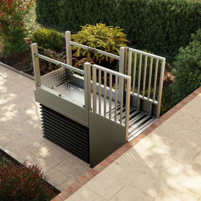 A modern outdoor platform lift is installed beside a paved walkway, providing step-free access between two levels in a landscaped garden area.