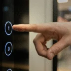 A hand is pressing the illuminated number one button on an elevator control panel.