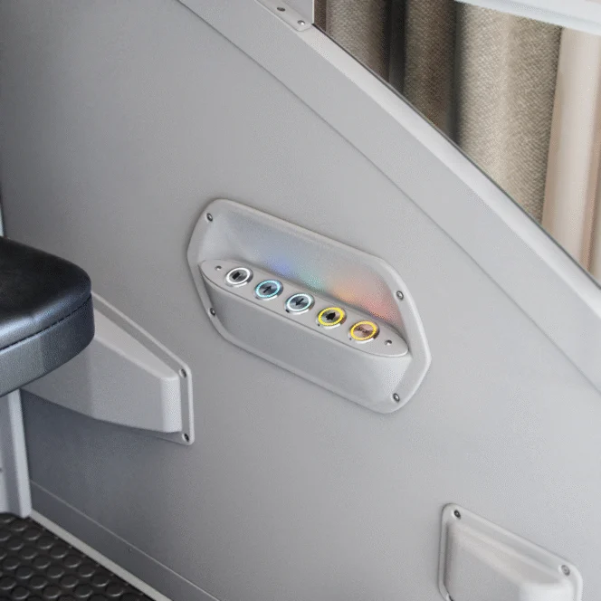 Close-up of a gray panel with six circular, color-coded buttons mounted on the side of a wall near a padded seat.