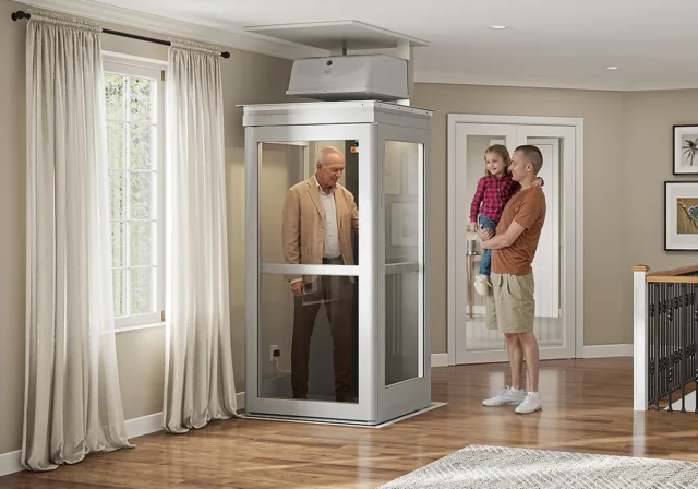An older man stands inside a home elevator while a man holding a young girl stands outside in a modern, well-lit living area.