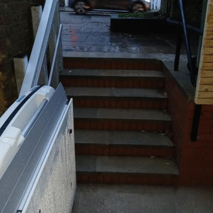 A stairway with a handrail and a closed wheelchair lift at the bottom, leading up to an outdoor sidewalk with a car passing by.