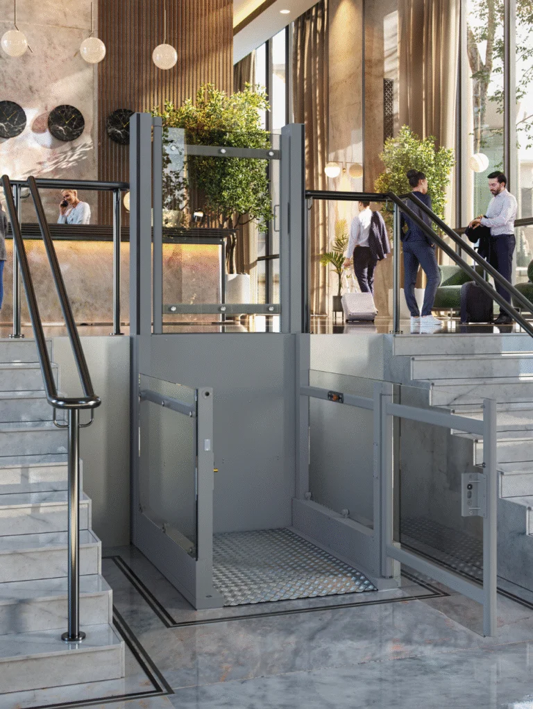 A modern hotel lobby with stairs, a reception desk, people interacting, and a wheelchair lift providing accessible entry between stair levels.