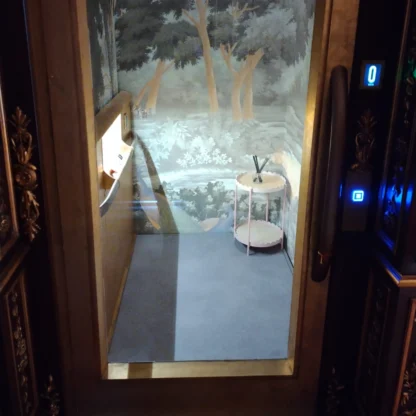 A small elevator with mirrored walls and a nature-themed mural, featuring a round side table with a decorative item and a control panel on the left.