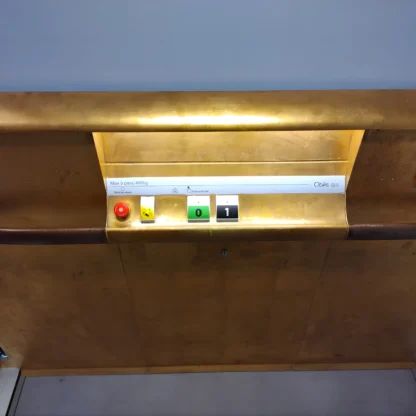 Gold-colored dumbwaiter control panel with a red emergency button, a key switch, and indicator lights displaying 0 and 1.