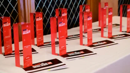 A table displays multiple red rectangular award trophies and certificates arranged in rows, set for an event.