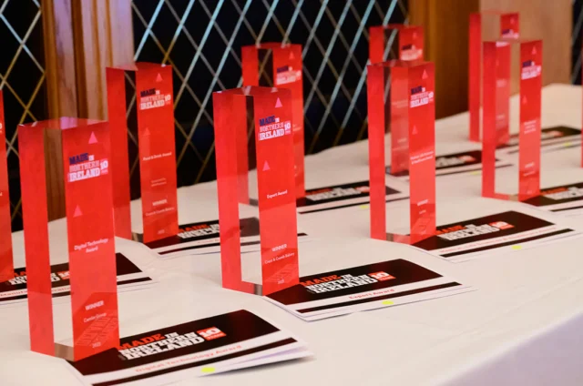 A table displays multiple red rectangular award trophies and certificates arranged in rows, set for an event.