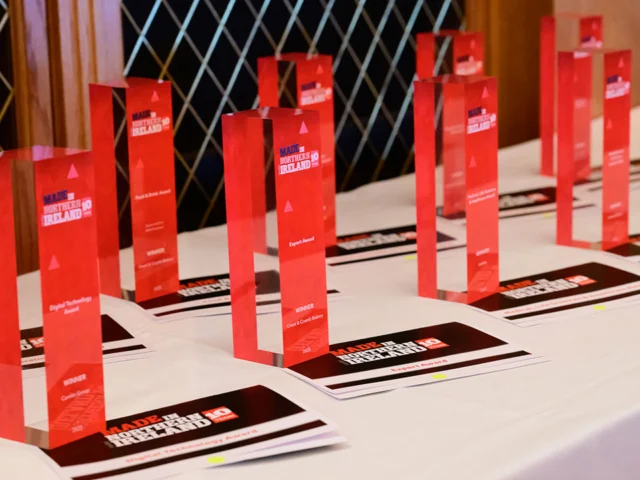 A table displays multiple red rectangular award trophies and certificates arranged in rows, set for an event.