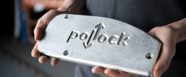 Person holding a metal plate with the word “Pollock” and up and down arrows engraved on it.