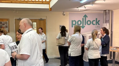 A group of people in white uniforms gather in a lobby area with a sign reading “Pollock Lifts” on the wall.